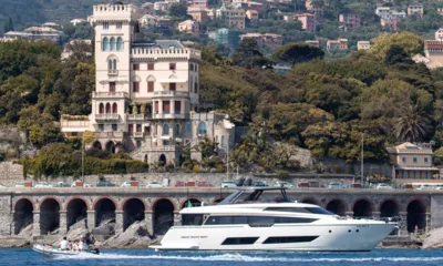 E3: Yacht in navigazione lungo una costa con muraglione ad archi, villa in stile castello e tender affiancato