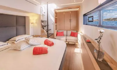 Looma: Helle Kabine mit Doppelbett, korallenroten Handtüchern, kleinem Sofa und langem Fenster mit Meerblick
