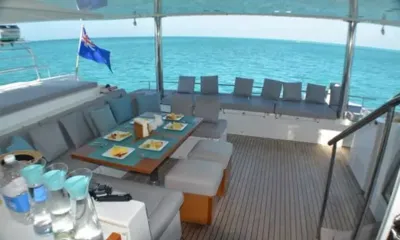 Amura II: Outdoor dining table set with plates of fruit on the shaded aft deck facing the sea