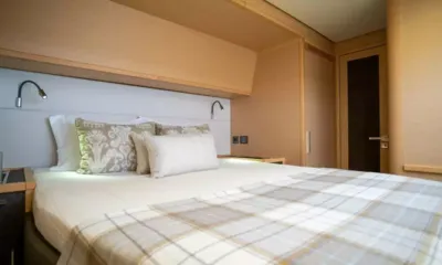 Ascension: Cabine avec lit double, coussins à motifs, plaid à carreaux, liseuses et lambris en bois clair