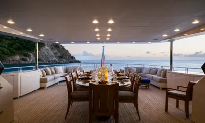 Balista: Deck de popa coberto com mesa de jantar posta e sofás ao anoitecer de frente para o mar