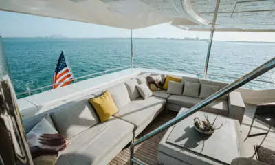 Bonus Round: Lounge sombreado no convés de popa com sofá cinza, almofadas e mesa de centro com vista para o mar