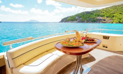 Casual: Mesa do convés de popa com travessas de comida ao lado de bancos creme com vista para o mar turquesa