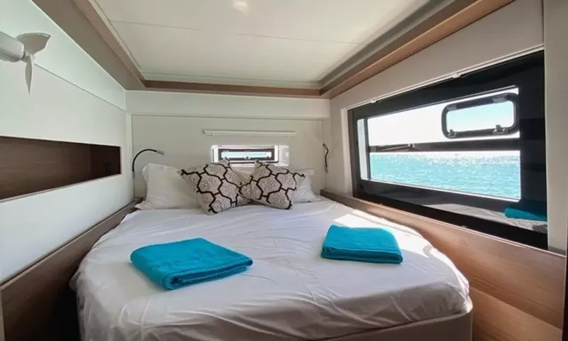 Sea Spirit 3: Cabine dupla clara com roupa de cama branca, toalhas azuis e uma janela para o mar