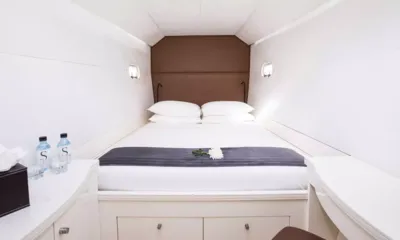 Magic Cat: White guest cabin with double bed, grey runner and bottled water on the side