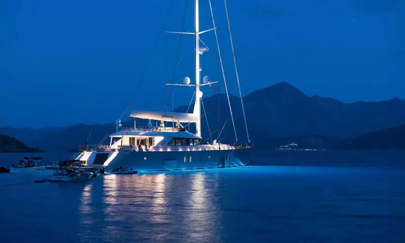 All About U 2: Sailing yacht at anchor at dusk with glowing blue underwater lights and tenders alongside