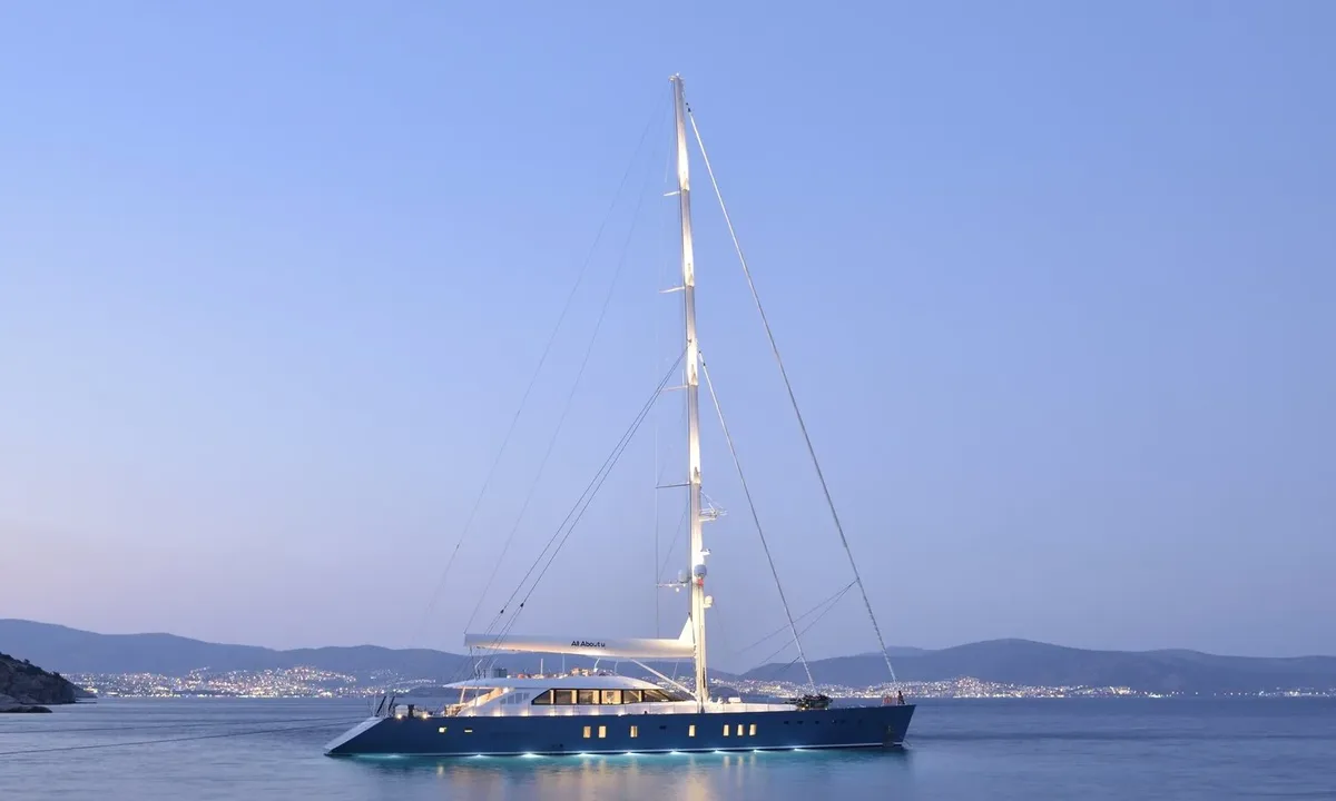 All About U 2: Single masted sailing yacht at anchor at dusk with underwater lights and a lit coastline behind