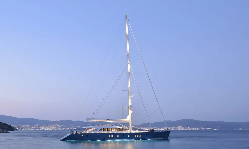 All About U 2: Single masted sailing yacht at anchor at dusk with underwater lights and a lit coastline behind