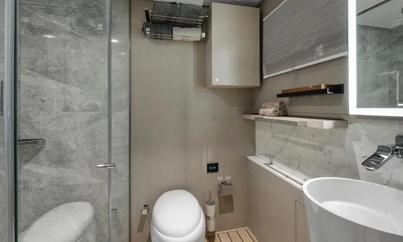 All About U 2: Bathroom with glass shower, toilet, towel rack and a white basin under a lit mirror