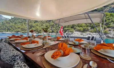 Queen of Makri: Mesa externa posta com pratos e guardanapos laranja sob uma cobertura junto a uma baía arborizada