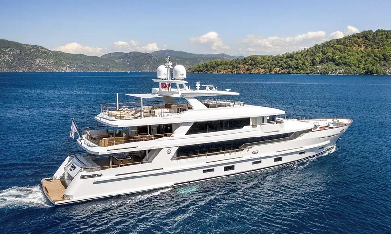 Sunrise: White motor yacht cruising on deep blue water past green wooded hills