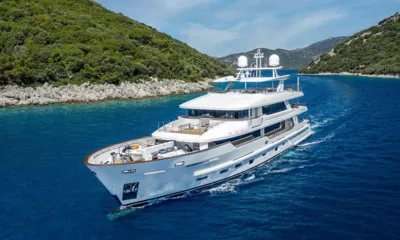 Sunrise: White yacht under way in a channel between green rocky shores