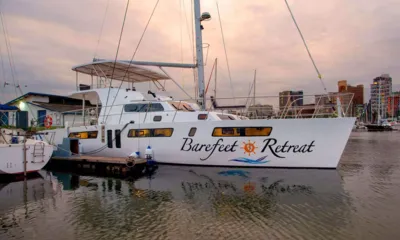 Barefeet Retreat: Catamarano bianco ormeggiato a una banchina della marina al crepuscolo, con edifici della città sullo sfondo