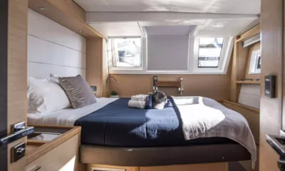 Colette: Cama de casal com colcha azul marinho e toalhas sob três janelas em uma cabine revestida de madeira