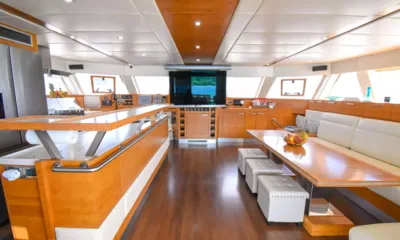 Excess: Salão claro com bancada de cozinha de madeira, mesa de jantar com banquetas brancas e uma tela grande