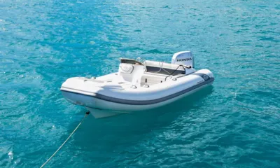 Excess: Bote auxiliar inflável branco com motor de popa amarrado a um cabo em água turquesa