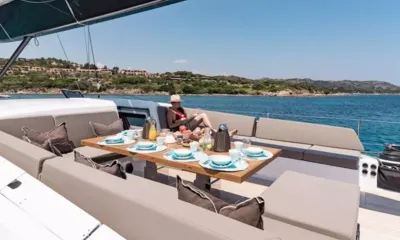 Neyina: Table du cockpit dressée pour le petit-déjeuner, entourée de banquettes rembourrées donnant sur une baie côtière