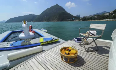 SL78: Plataforma de popa com cadeira, chapéu e bandeja de suco ao lado de uma piscina flutuante, uma prancha de stand up paddle e colinas verdes