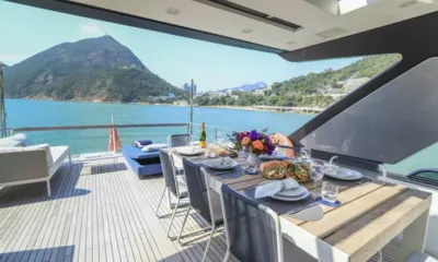 SL78: Mesa do flybridge posta com frutos do mar, vinho e flores com vista para uma baía e uma montanha verde