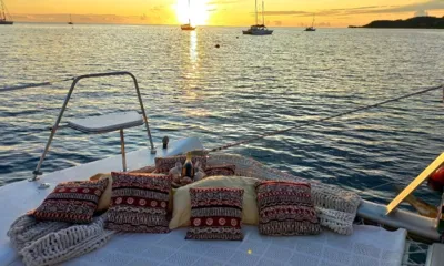 XXX: Almofadas e cobertores sobre a rede da proa voltada para um pôr do sol sobre um ancoradouro