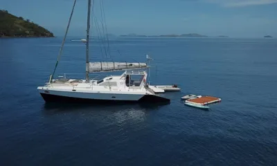 XXX: Catamarã a vela ancorado em águas azuis calmas com bote auxiliar, pranchas de paddle e tapete flutuante por perto