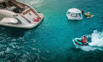 YCM120: Pilota su una moto d'acqua vicino alla poppa dello yacht, con isola galleggiante con baldacchino, tavole da SUP e tubo gonfiabile