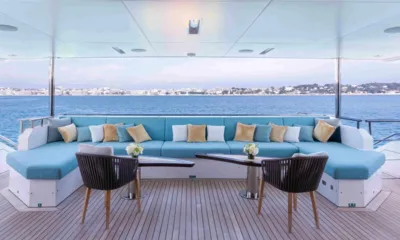 Charade: Lounge do convés de popa com sofá azul curvo, duas mesas e cadeiras voltadas para o mar