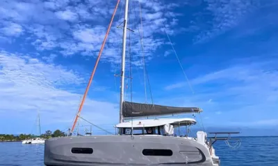 Here Matai: Catamarã de vela cinza ancorado sob um mastro alto e um céu azul dramático com nuvens esparsas