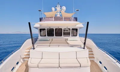 3D: シェードセイルの下にクッション付きシートとサンパッドがあるフォアデッキ。両側に穏やかな青い海が広がる