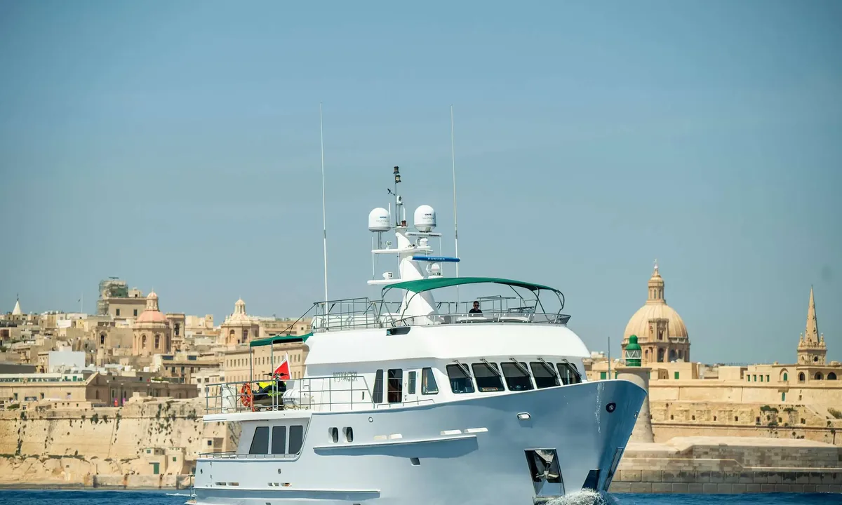 Voyager: White motor yacht under way in front of a historic stone city with domes