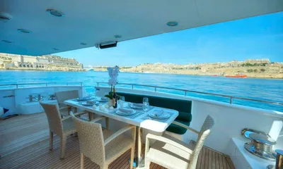 Voyager: Shaded aft deck table set for a meal with wicker chairs and harbour views