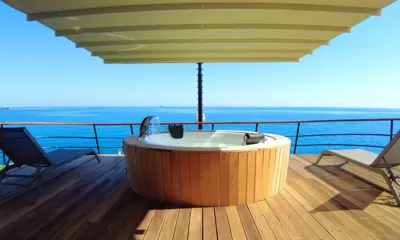 Limitless II: Jacuzzi redondo revestido de madeira entre duas espreguiçadeiras em um deck sombreado voltado para o mar aberto