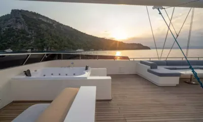 De Love: Top deck jacuzzi and lounge seating facing a sunset over a wooded headland