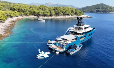 King Benji: Blue yacht anchored in a wooded cove with tender, floating platform and water toys astern
