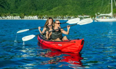 NDS Evolution: Two women paddling a red inflatable kayak on blue water near a green shore