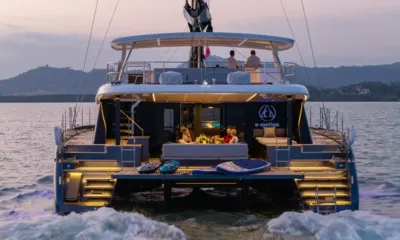 E Motion: Stern of the catamaran at dusk with guests dining on the lit aft deck