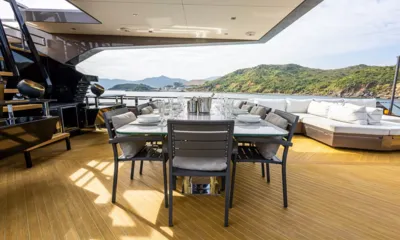 Rock: Shaded deck dining table with grey chairs next to a large white sofa overlooking green hills
