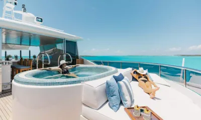 Odyssea: Dois hóspedes relaxando em um jacuzzi no deck e em um colchonete de sol acima da água turquesa