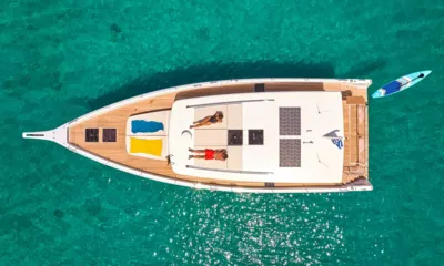 N ICE: Vista aérea do iate em águas turquesa com pessoas tomando sol no teto e uma prancha de stand up paddle