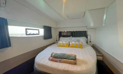 Rise: Cabine dupla com roupa de cama branca, almofadas amarelas e uma janela no casco