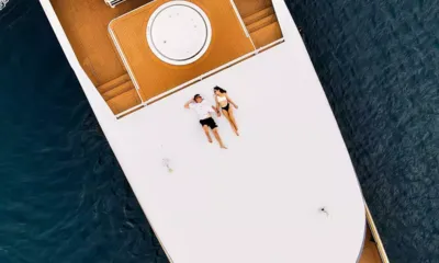 Velocean: Vista aérea de um casal deitado no deck de proa branco sobre o mar azul escuro