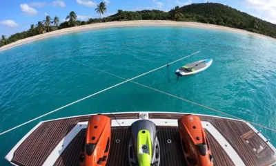 Hecht Yeah: Scooters aquáticos na plataforma de popa com uma prancha de stand up paddle flutuando perto de uma praia com palmeiras