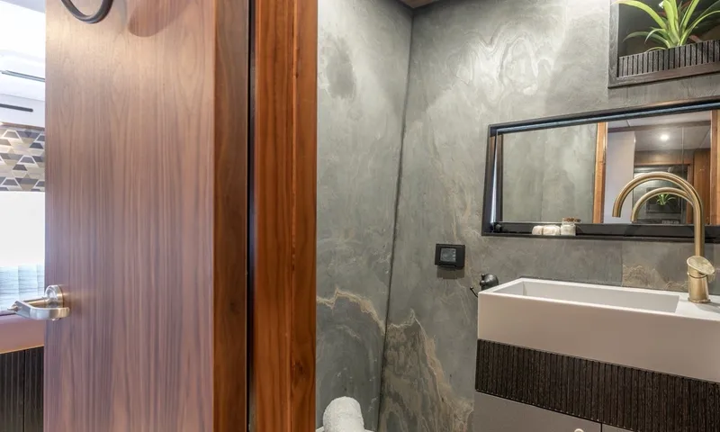 Hani I: Ensuite with slate stone walls, white basin and brass tap beside wooden door