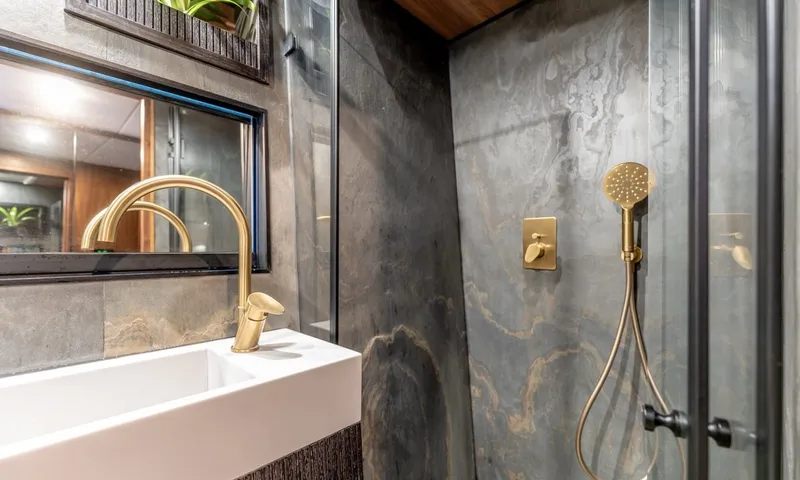 Hani I: Stone walled bathroom with brass basin tap and handheld shower behind glass