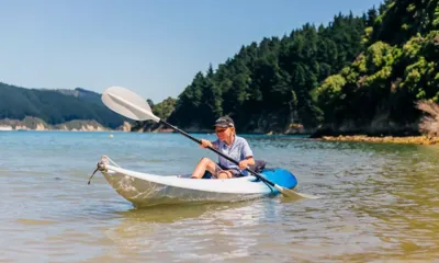 Indian Summer: Bambino che pagaia su un kayak a fondo trasparente in acque basse vicino a una riva boscosa