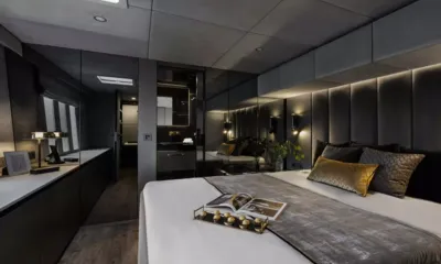 XMotion: Cabine cinza com cama de casal, cabeceira estofada, parede espelhada e porta para o banheiro privativo