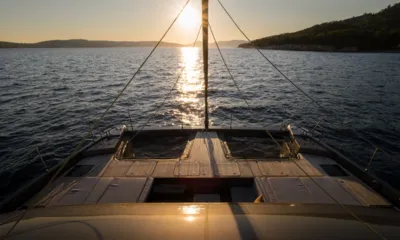 Ahalya: Convés de proa de teca com redes de trampolim voltado para o sol se pondo sobre águas calmas e colinas