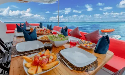 Misraab: Deck table laid with fruit, salad and pasta beside red seating overlooking turquoise sea
