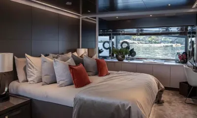 Ella: Cama de casal com almofadas cinza e vermelhas ao lado de uma janela ampla com vista para a água