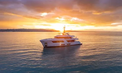 Pazienza: Iate branco ancorado em mar calmo ao pôr do sol com nuvens douradas e litoral distante
